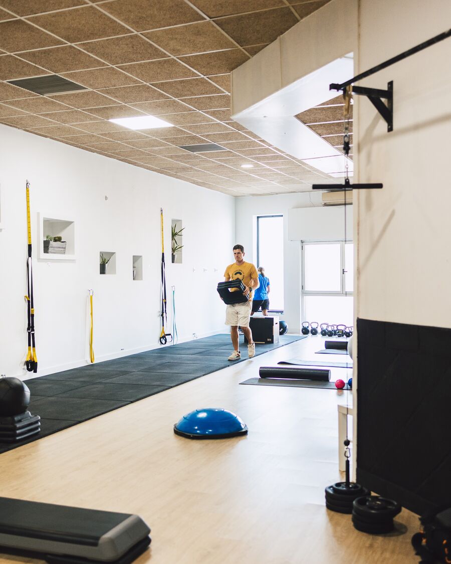 La sala de entrenamiento: suelo de madera, zona de caucho, TRX en la pared y material ordenado.